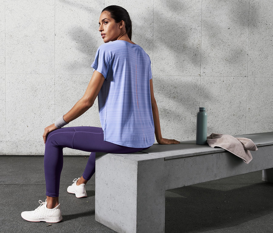 Frau sitzt auf einer Betonbank und trägt ein violett meliertes Sportshirt.