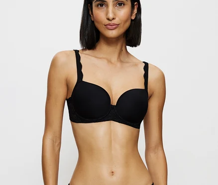 Eine Frau trägt einen schwarzen Triumph Amourette WP BH und schwarze Spitzen-Slips, blickt nach vorne.