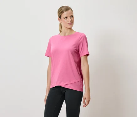 Frau posiert in einem rosa T-Shirt und schwarzen Hosen.