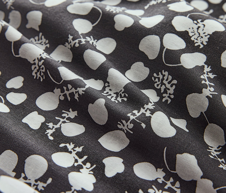 Nahaufnahme eines Stoffes mit weißen Blüten und Punkten auf dunklem Grund.