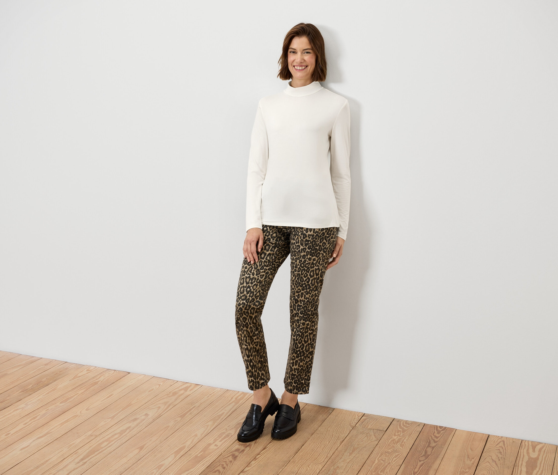 Frau posiert in einem cremefarbenen Langarmshirt und einer Hose mit Animal-Print.