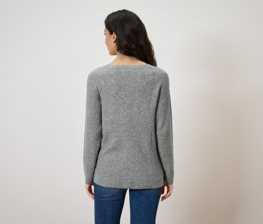 Rückansicht einer Frau mit dunklen Haaren, die einen grauen Pullover und blaue Jeans trägt.