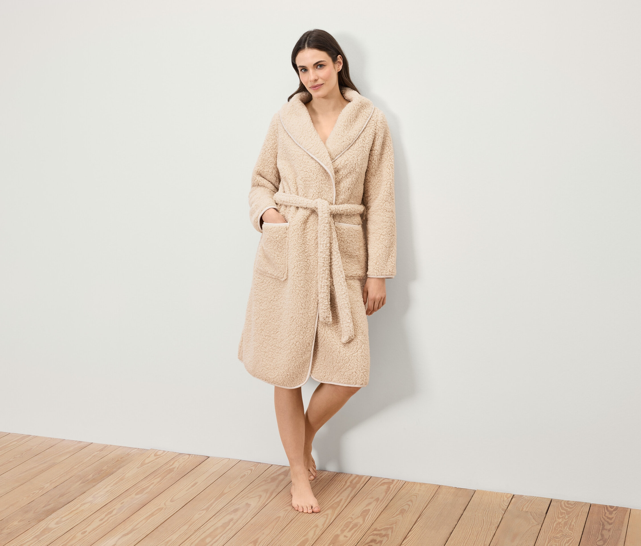 Eine Frau steht und trägt einen flauschigen Bademantel mit Gürtel.