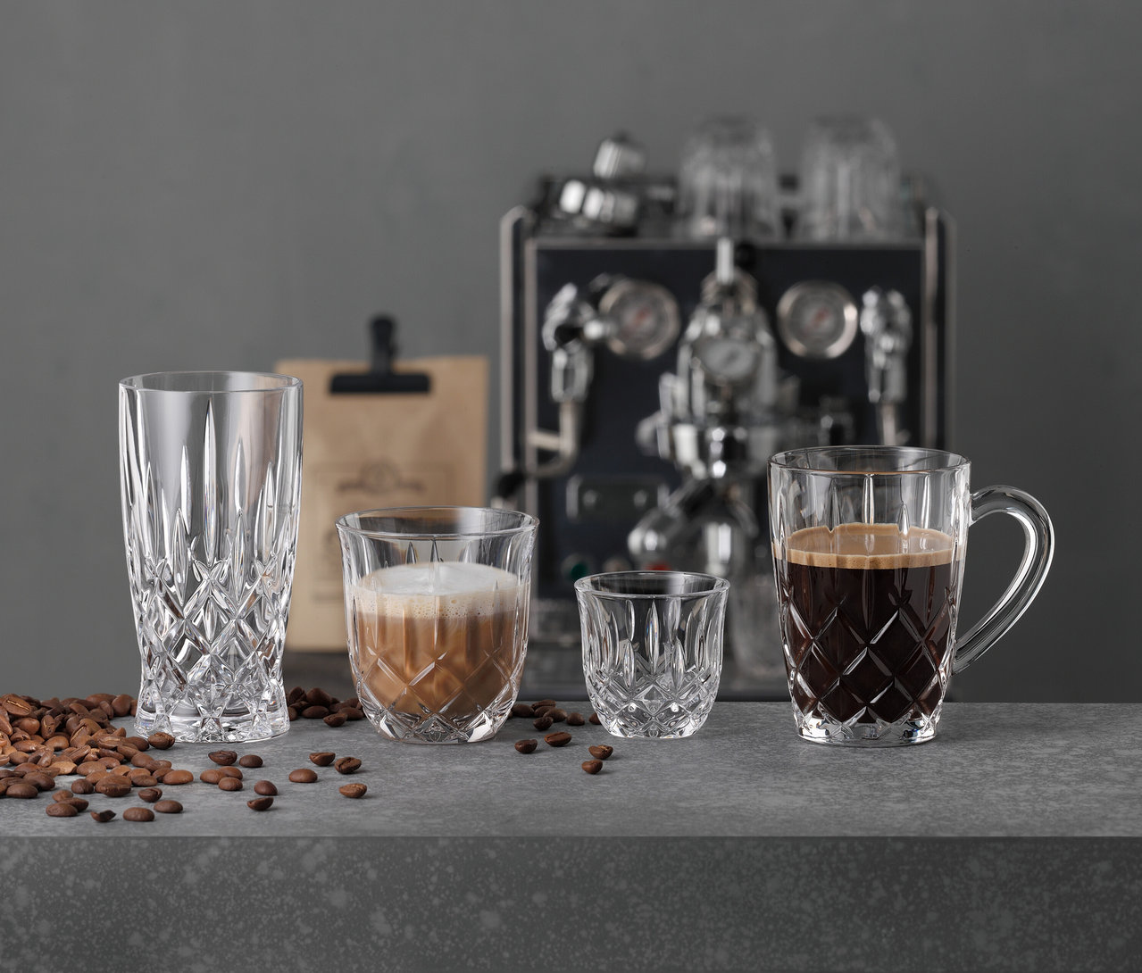 Vier Gläser, inklusive 6 Nachtmann Latte-Macchiato-Gläser »Noblesse«, stehen auf einer Theke mit Kaffeebohnen; eine Kaffeemaschine ist im Hintergrund.