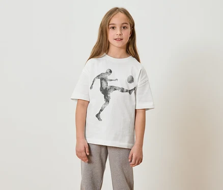 Mädchen mit langem Haar trägt ein weißes T-Shirt mit einem Fußballspieler-Aufdruck und graue Jogginghose.