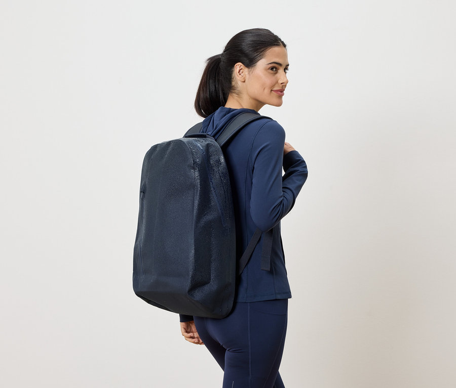 Frau mit marineblauem Trainingsanzug und marineblauem Rucksack, der über ihre Schulter hängt, blickt über ihre Schulter.