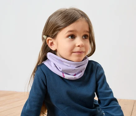 Mädchen mit braunen Haaren und Haarspange trägt ein blaues Langarmshirt und ein lila Halstuch mit Einhornmuster.