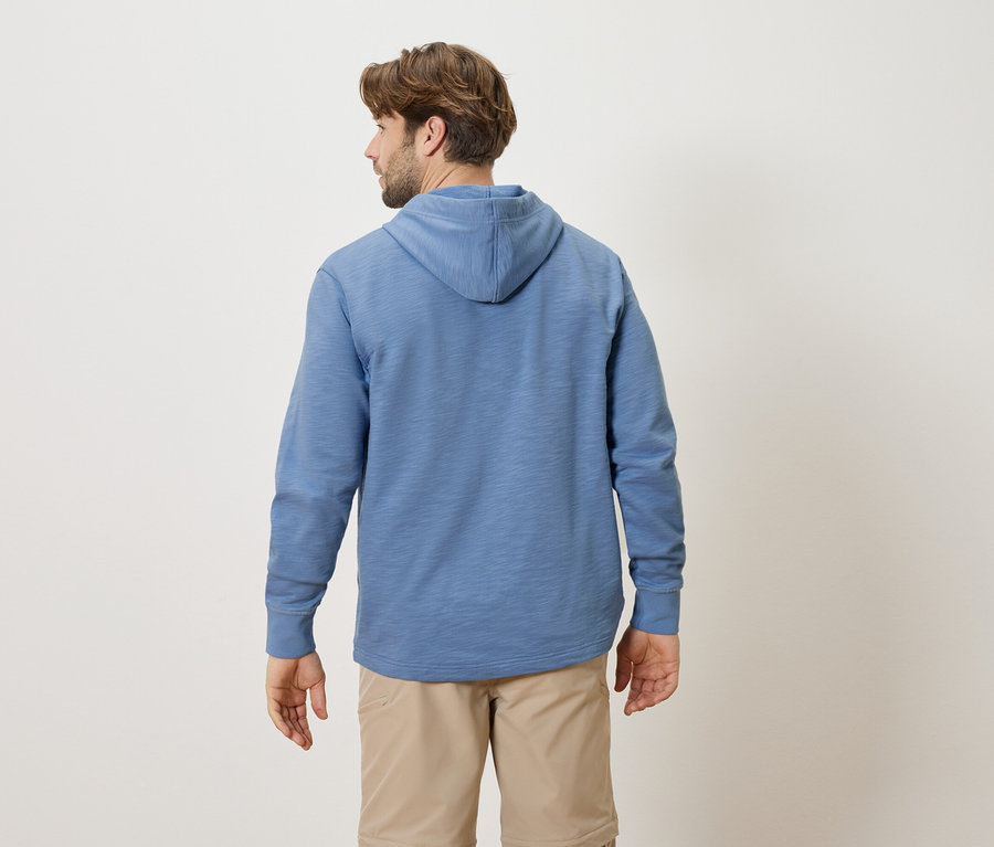 Ein Mann von hinten, der einen blauen Kapuzenpullover und beige Shorts trägt.