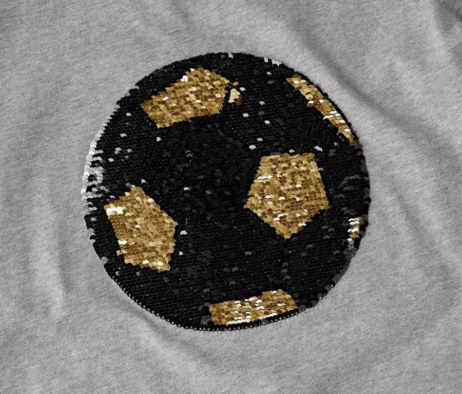 Auf einem grauen Stoff ist ein Fußball aus schwarzen und goldenen Pailletten abgebildet.