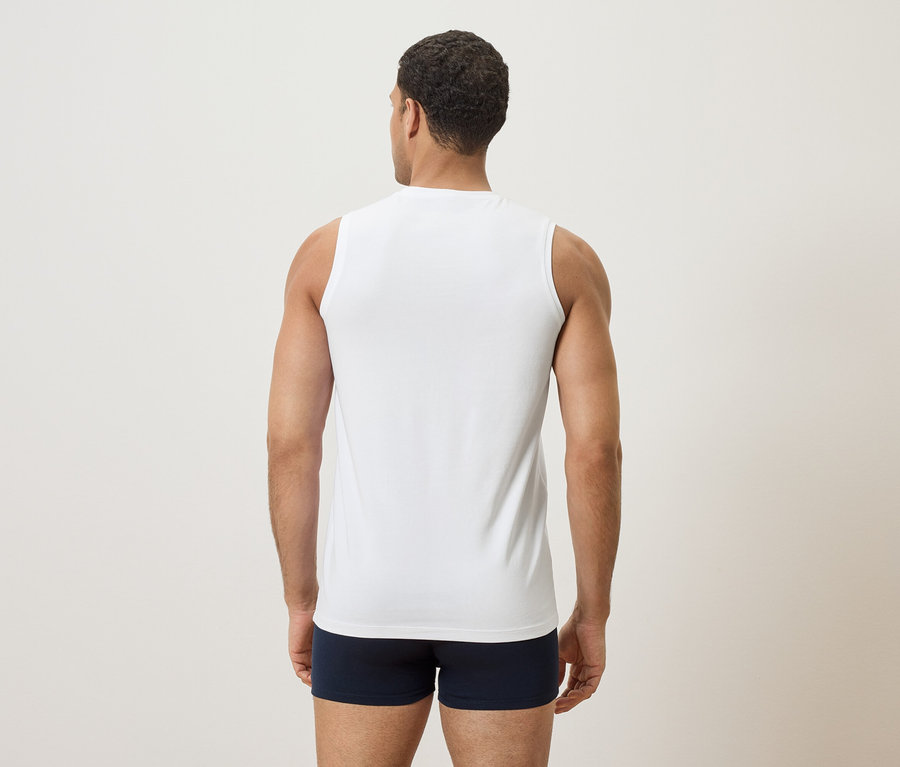 Mann von hinten, trägt ein weißes Tanktop und blaue Boxershorts.