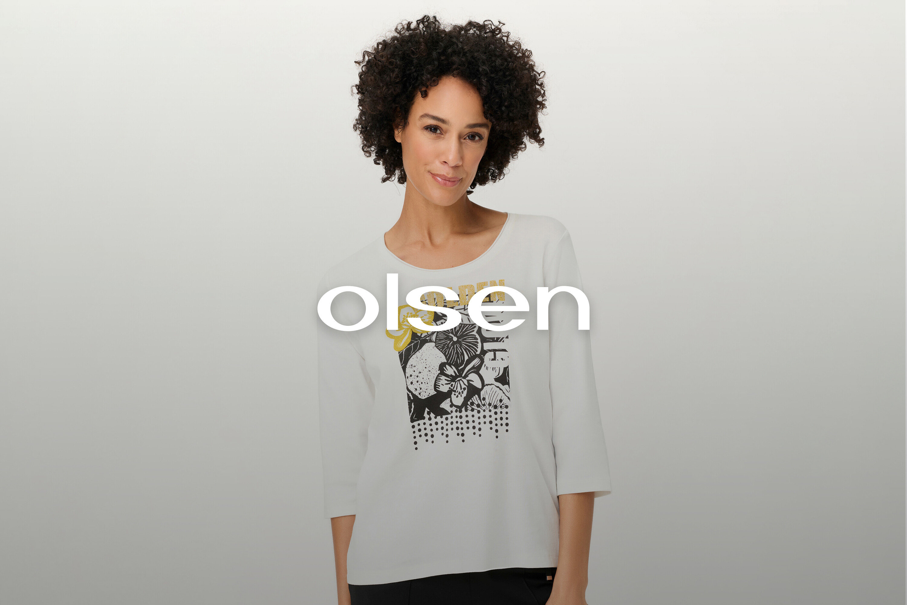 Frau mit lockigem Haar trägt ein weißes Langarmshirt mit Blumenmuster.