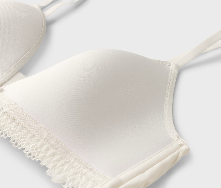 Detailansicht eines weißen BHs mit Spitze und schmalen Trägern.