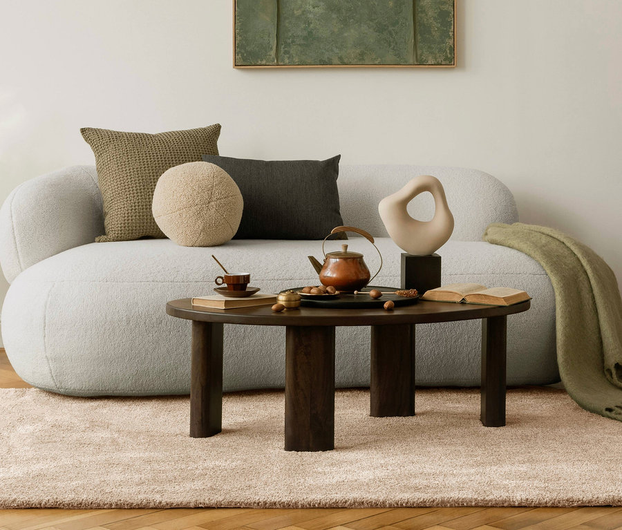 Wohnzimmer mit beigem Teppich »Jane« und Sofa mit Kissen. Auf einem runden Tisch stehen eine Teekanne, eine Tasse und Deko.