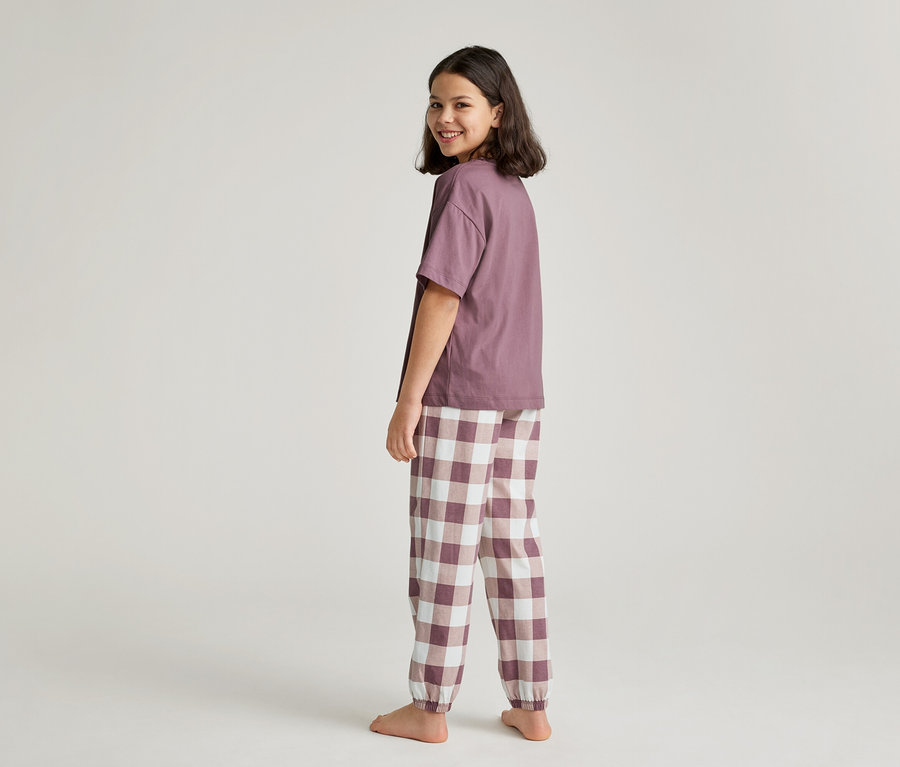 Ein junges Mädchen blickt über die Schulter und trägt ein lila T-Shirt und eine karierte Hose.