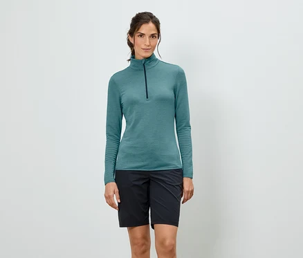 Frau trägt ein türkisfarbenes, langärmeliges Shirt mit Reißverschluss und schwarze Shorts.