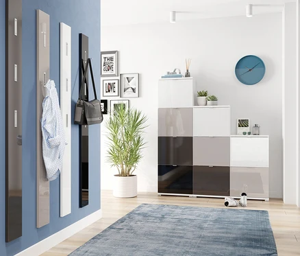 Vier Garderobenpaneele an blauer Wand: dunkelgrau, hellgrau mit Hemd, weiß und ein schwarzes Garderobenpaneel mit silberfarbenen Haken und Tasche. Modulare Aufbewahrung, Pflanze, blauer Teppich.