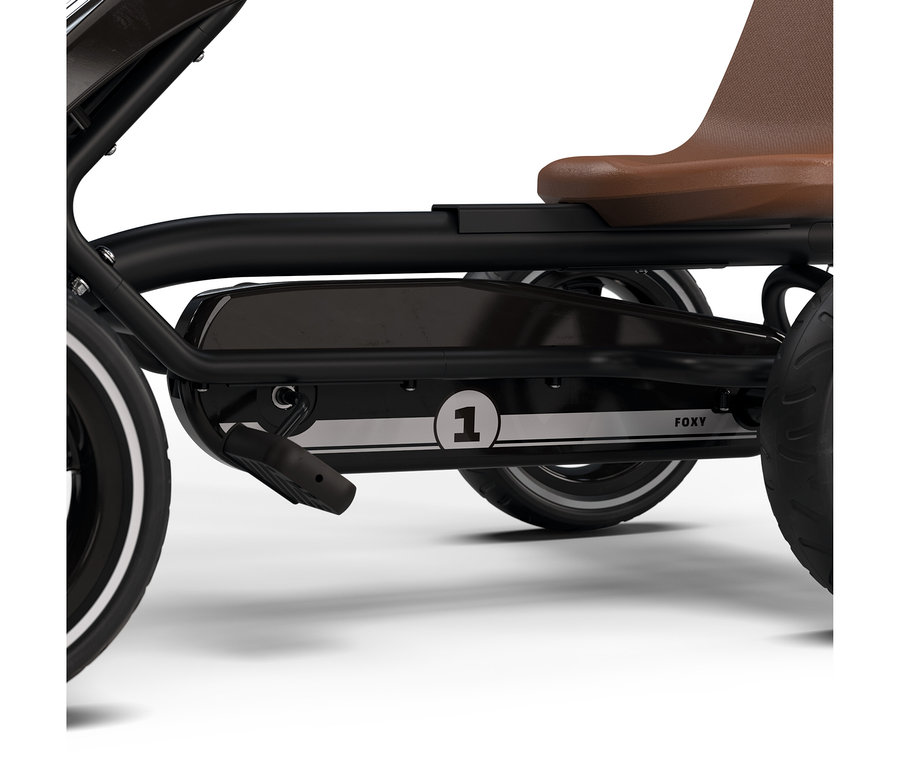 Nahaufnahme eines schwarzen Tretfahrzeugs mit braunem Sitz, einem Pedal und einem silbernen Streifen mit der Nummer „1“ und dem Schriftzug „FOXY“ an der Seite.