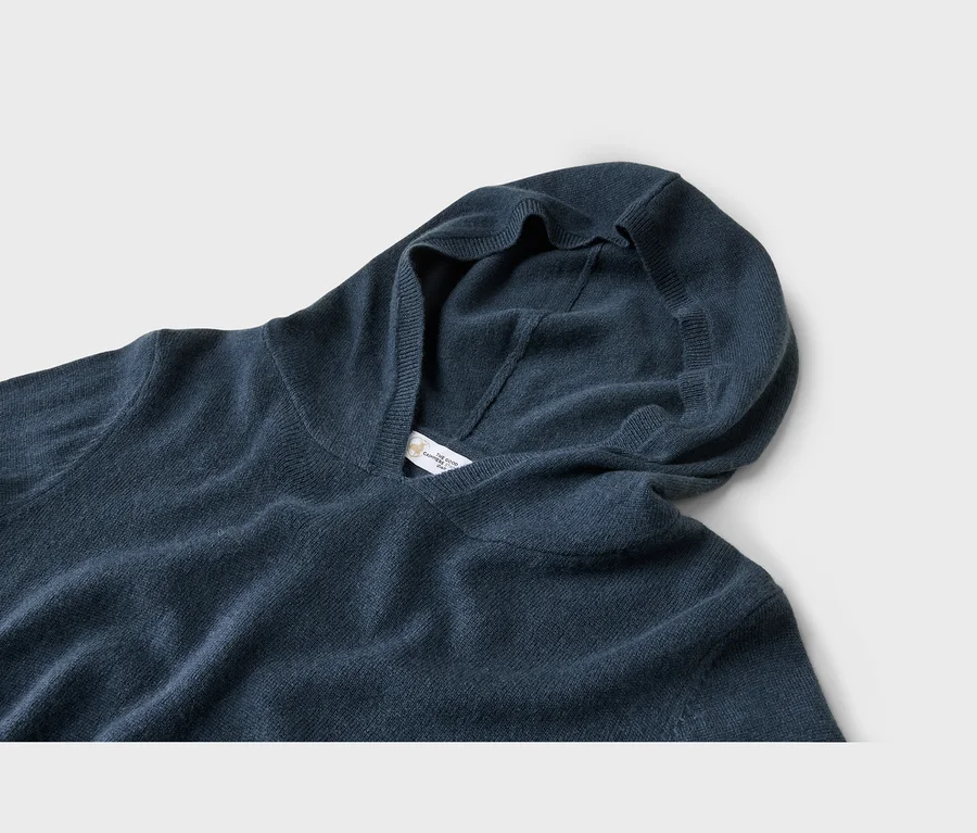 Nahaufnahme eines dunkelblauen Strickhoodies, der die Kapuze und ein weißes Etikett mit „THE GOOD CASHMERE STANDARD“ im Kragen zeigt.