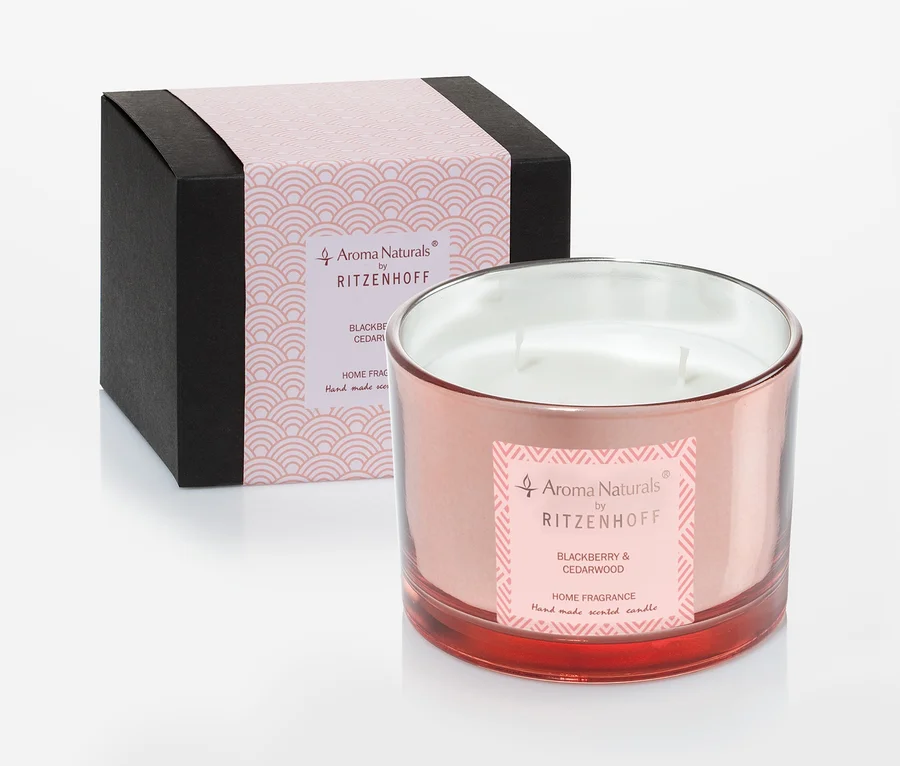Dekorative Kerze im rosafarbenen Glas mit Etikett steht neben einer schwarzen Schachtel mit rosa Details.