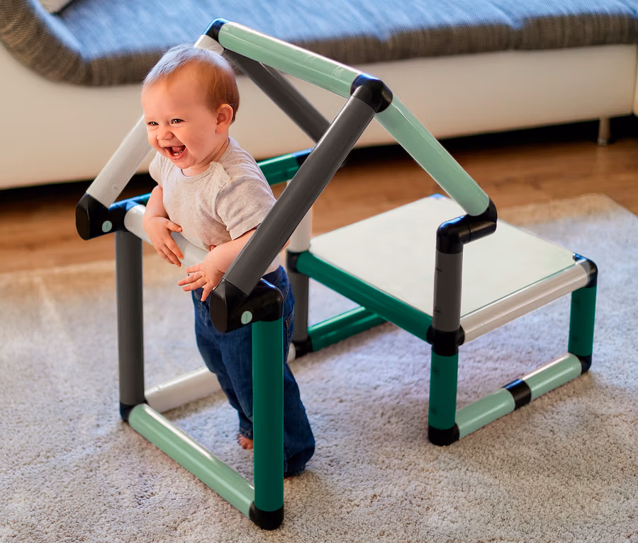 Ein lachendes Baby hält sich an einem mintfarbenen Quadro-Home-BEGINNER-Set in Grün, Grau und Weiß fest.