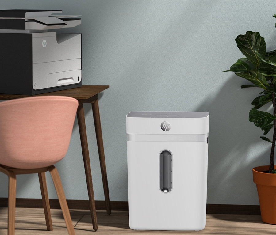 Ein weißer HP OneShred 12CC Aktenvernichter steht auf einem Holzboden neben einem Tisch mit einem Drucker.