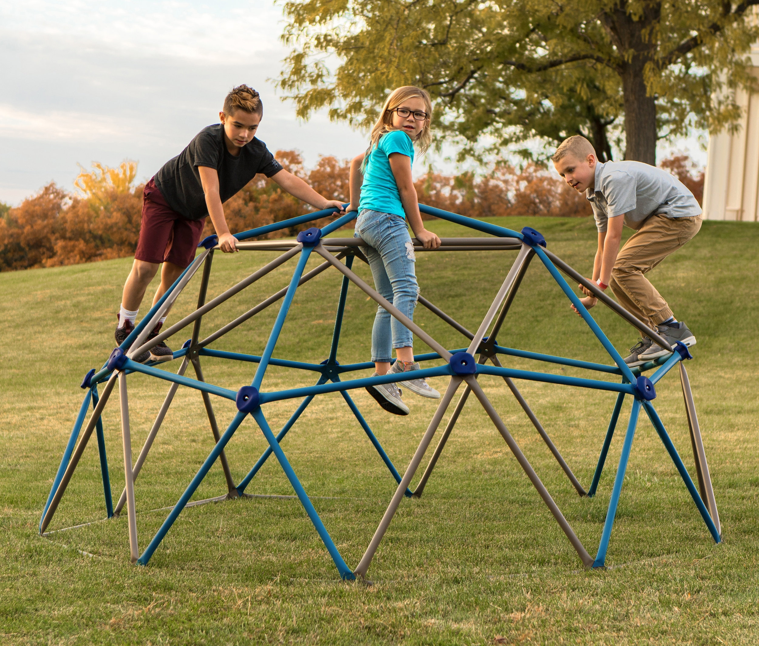 Drei Kinder spielen auf einem kleinen blau-grauen LIFETIME-Klettergerüst »Geodome« auf einer Rasenfläche.