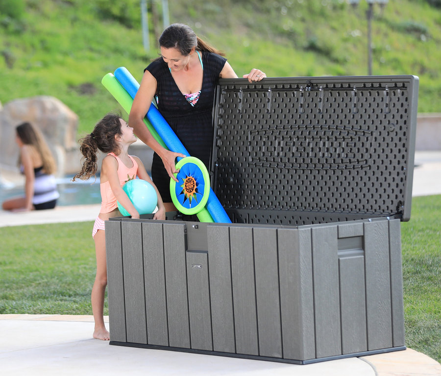 Eine Frau legt Strandspielsachen in eine Auflagenbox, ca. 570 l, während ein kleines Mädchen sie ansieht.