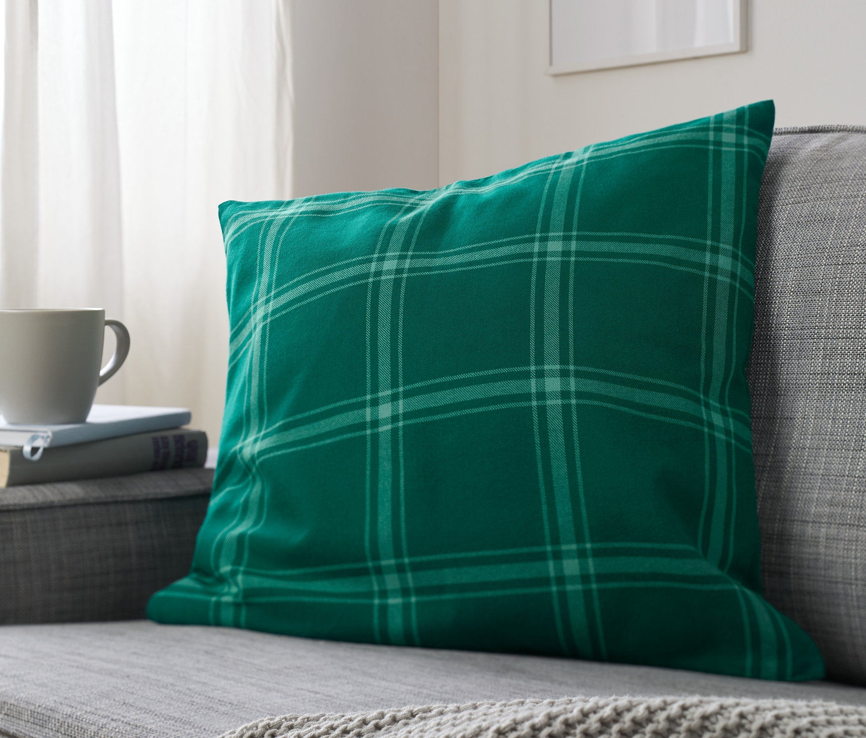 Ein grün karierter Dekokissenbezug liegt auf einem grauen Sofa.