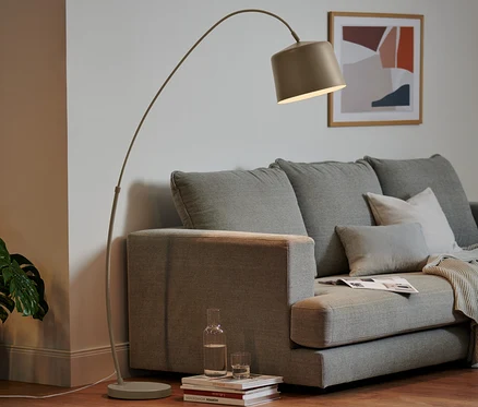 Cremefarbene Stehleuchte aus Metall neben grauem Sofa im Wohnzimmer.