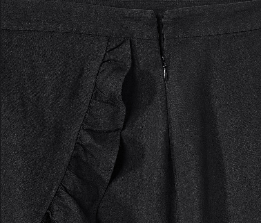 Detailansicht eines schwarzen Rocks in Wickeloptik mit Rüschen und Reißverschluss.