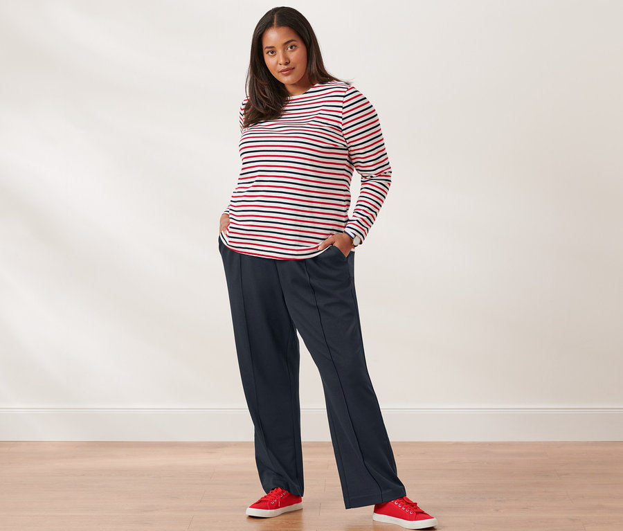 Eine Frau posiert in einem gestreiften Langarmshirt, einer Sweathose, Canvas-Sneakers und einer Quarz-Armbanduhr aus Edelstahl.