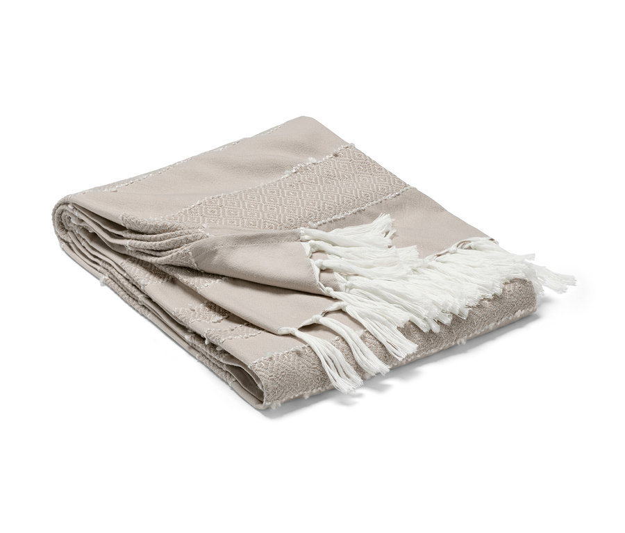 Eine beige Wohndecke mit dekorativen Fransen liegt gefaltet.