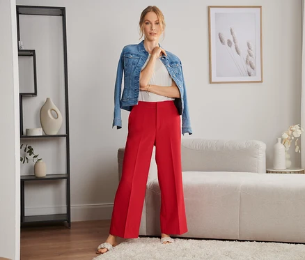 Frau posiert in Webhose, weißem Top und Jeansjacke in einem Wohnzimmer.