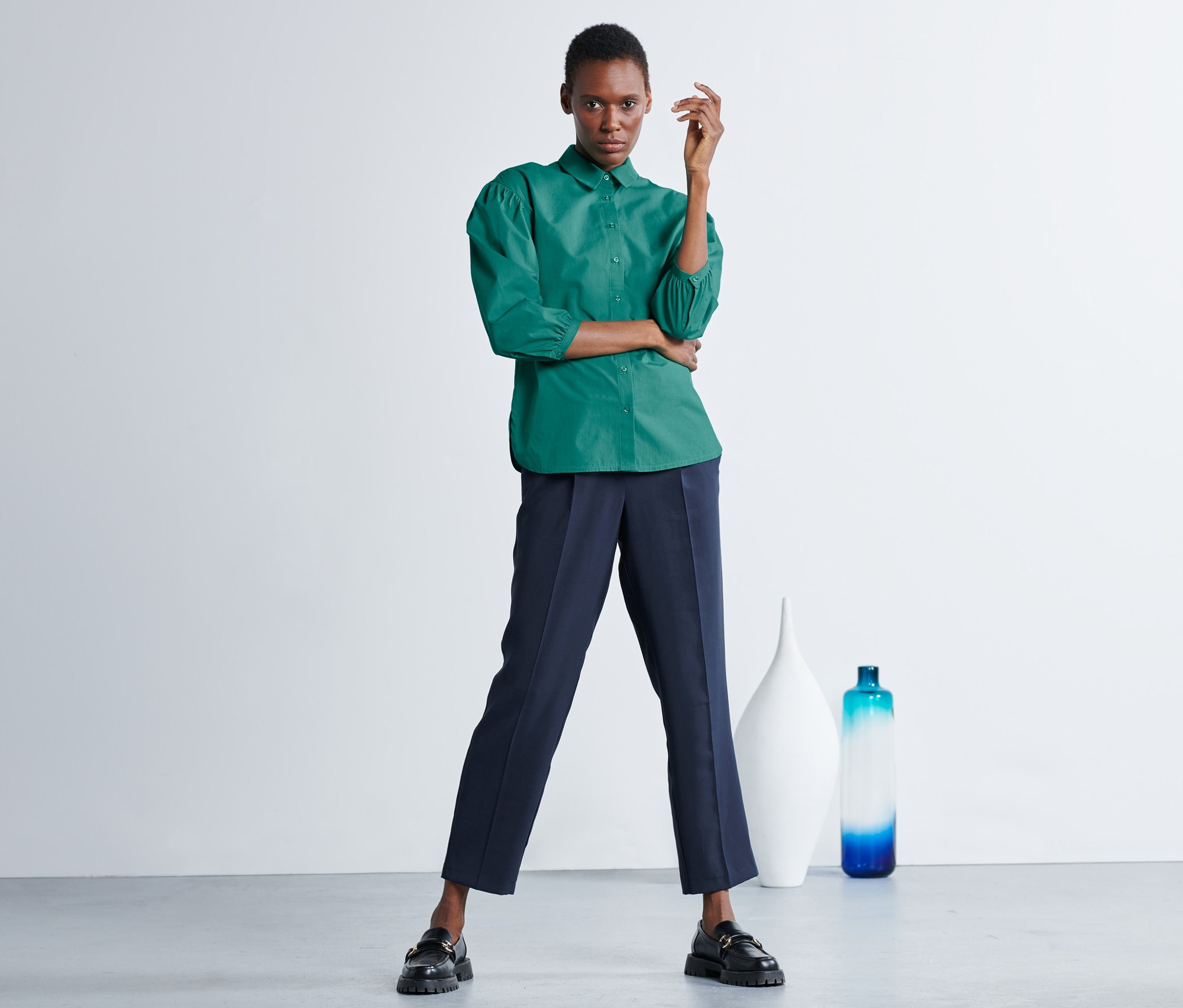 Frau posiert in grüner Hemdbluse mit Puffärmeln und dunkelblauer Hose.