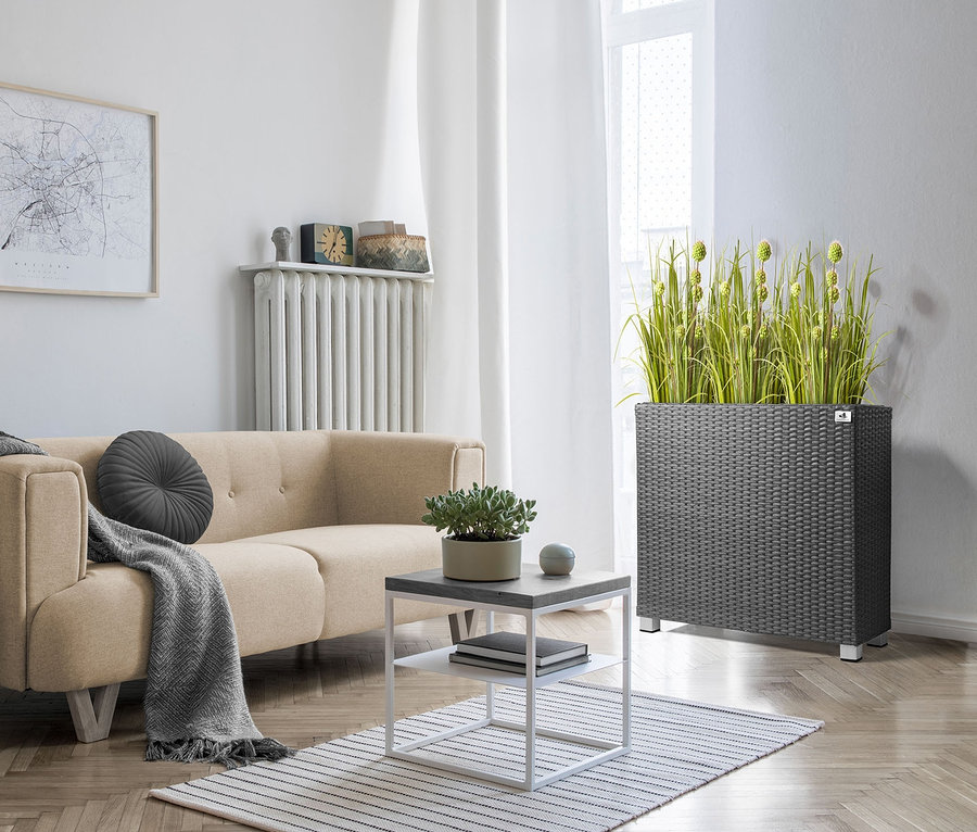 Wohnzimmer mit beigem Sofa, grauem Pouf und anthrazitfarbenem 2-in-1-Pflanzgefäß-und-Raumteiler aus Polyrattan.