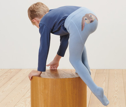 Ein Kind stützt sich auf einen Holzhocker, es trägt eine blaue Strumpfhose mit einem Hasenbild am Po. Auf dem Boden liegt ein Plüschtier. 2 Baby-und-Kleinkind-Strumpfhosen.