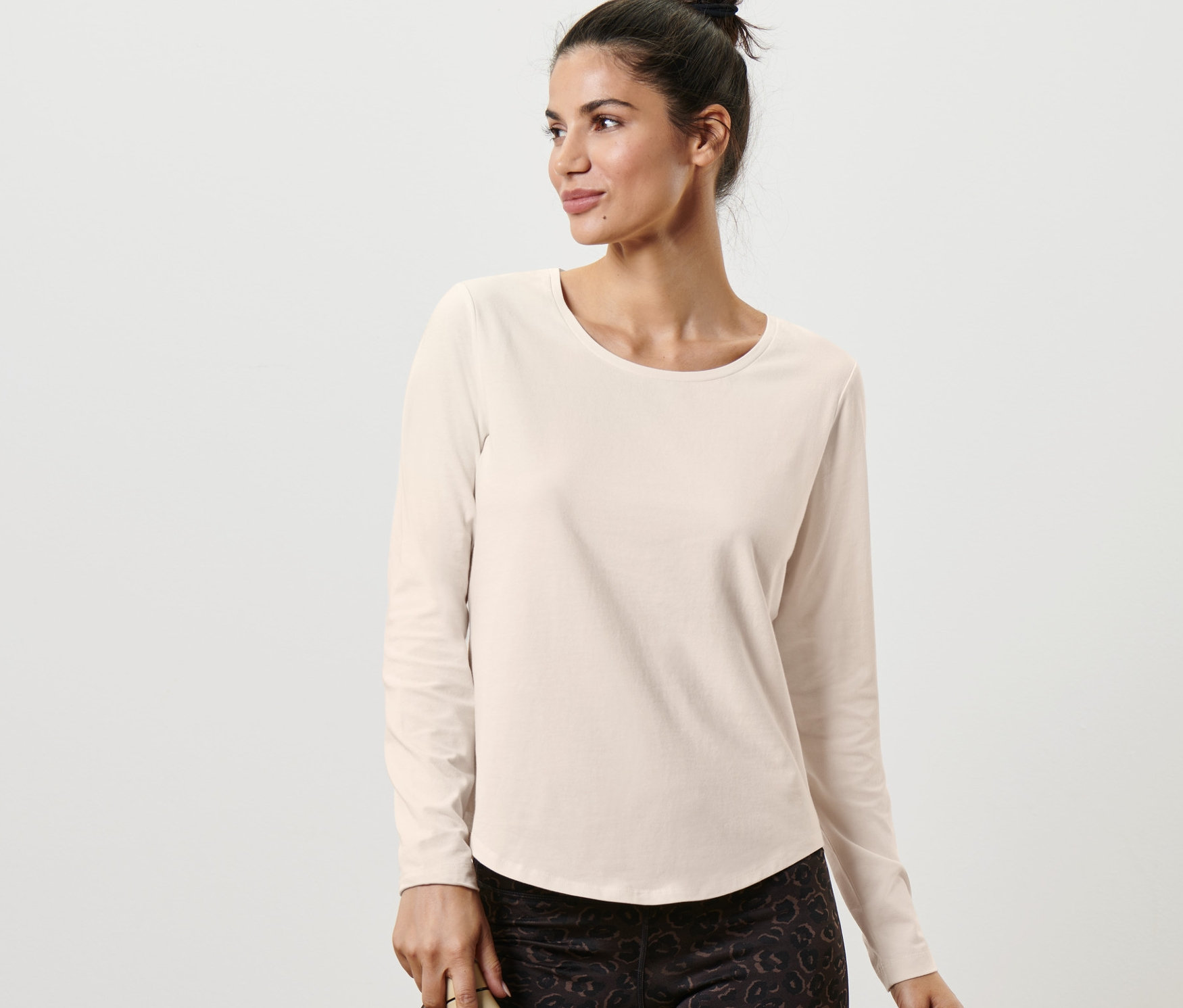 Frau posiert in einem Langarm-Sportshirt in Offwhite und hält eine Wasserflasche.