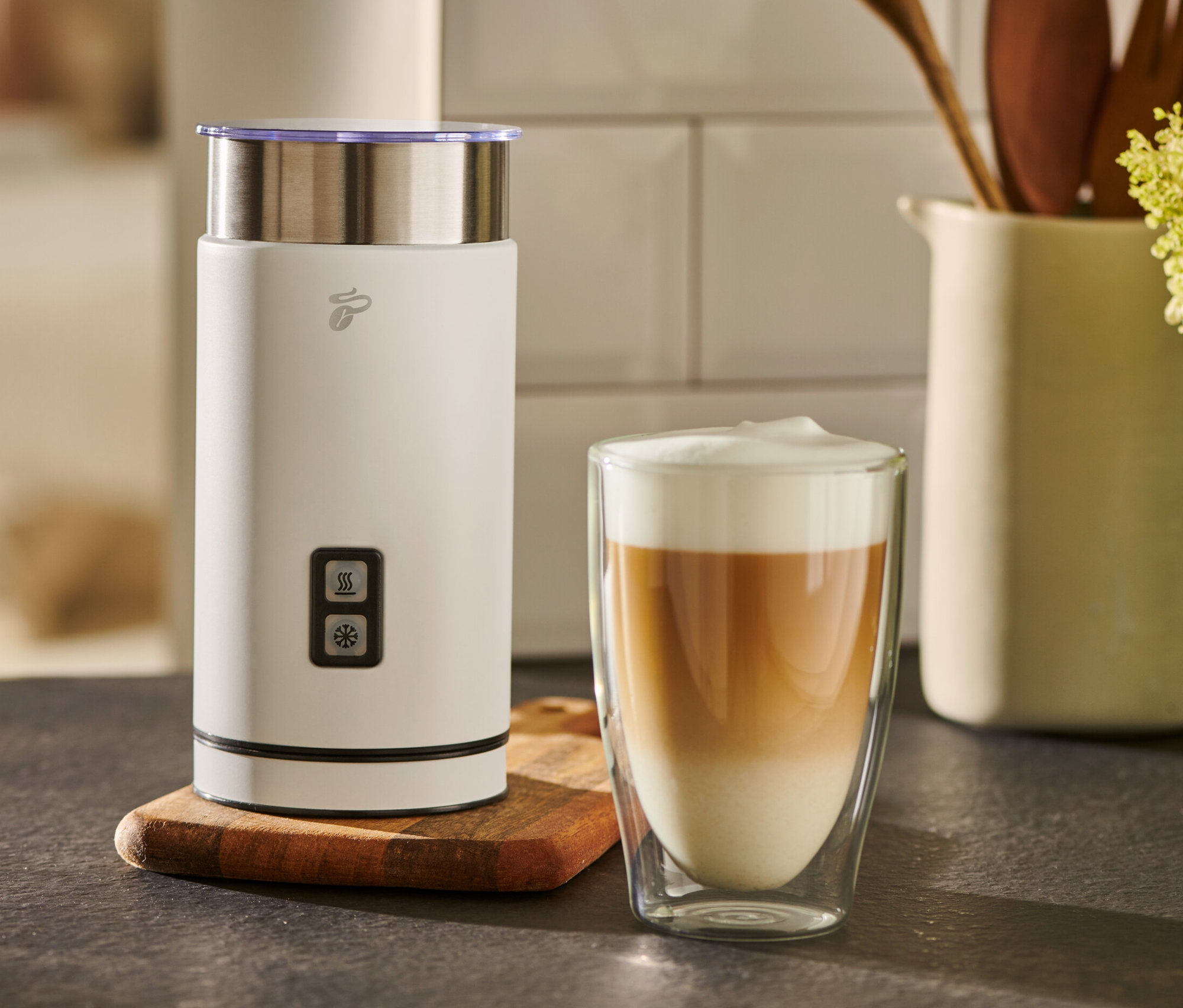 Ein weißer elektrischer Milschaufschäumer steht neben einem Glas Milchkaffee.