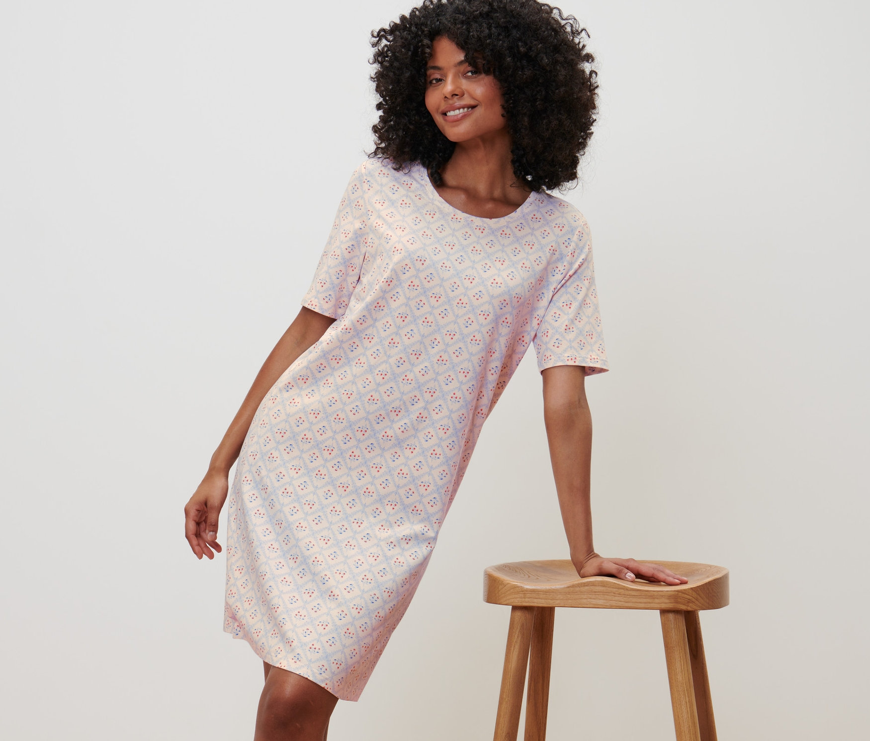 Frau posiert im Nachthemd mit kurzen Ärmeln, sich an einen Holzstuhl anlehnend.