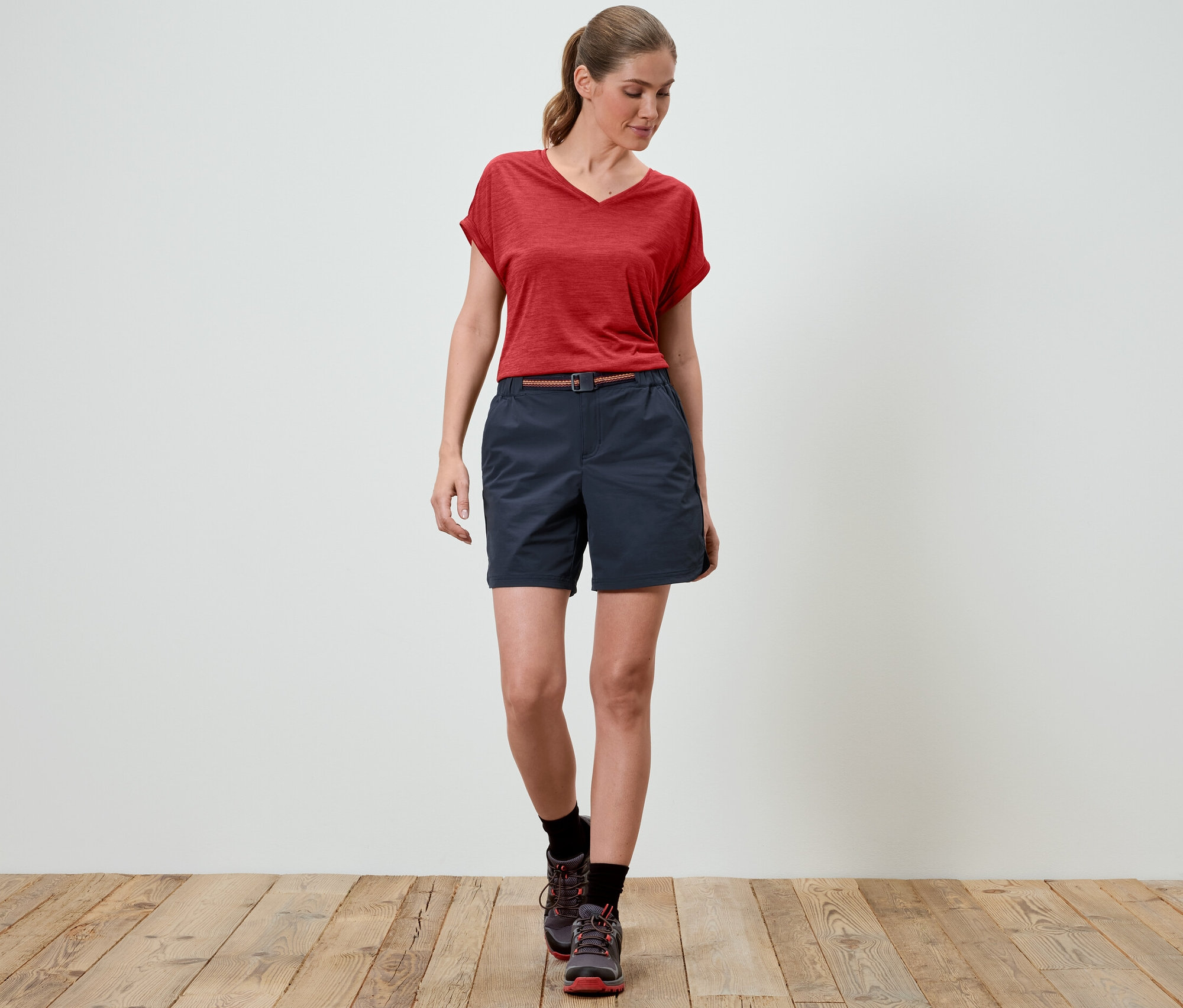 Eine Frau geht und trägt Funktionswandershorts und ein rotes T-Shirt.