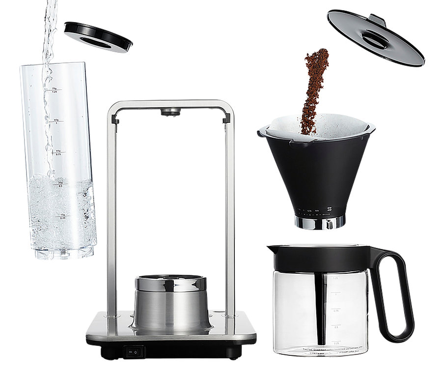 Wasser wird in den Messbecher der Kaffeemaschine gegossen. Gemahlener Kaffee wird in den Filter gegossen. Eine Karaffe steht neben der Kaffeemaschine.