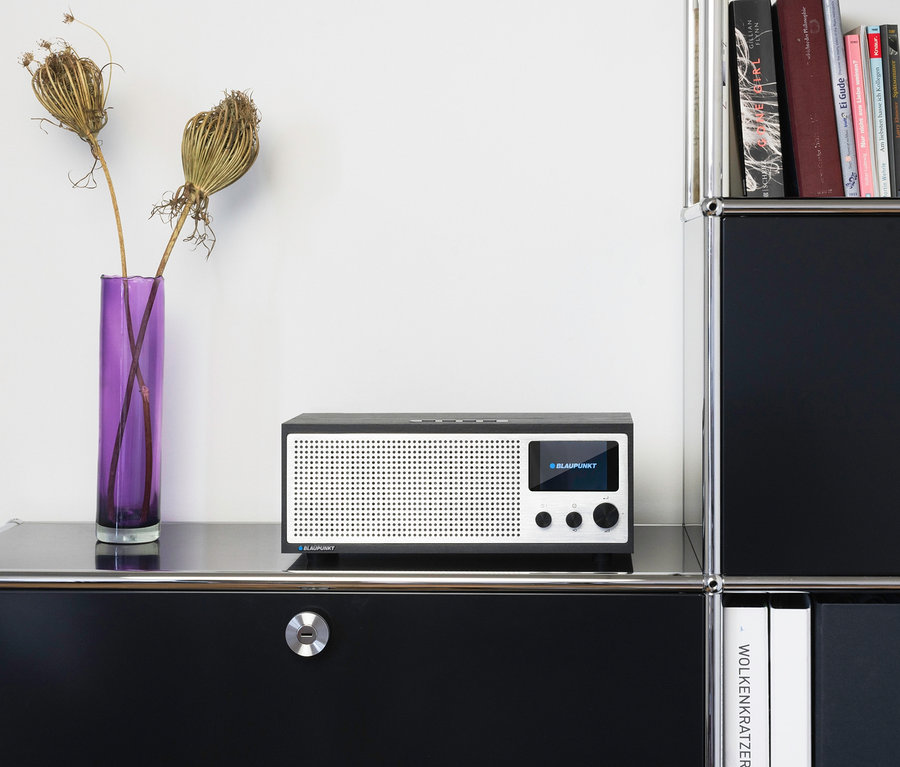 Ein schwarz-weisses Blaupunkt Internetradio »Napoli« steht neben einer lila Vase mit getrockneten Blumen.