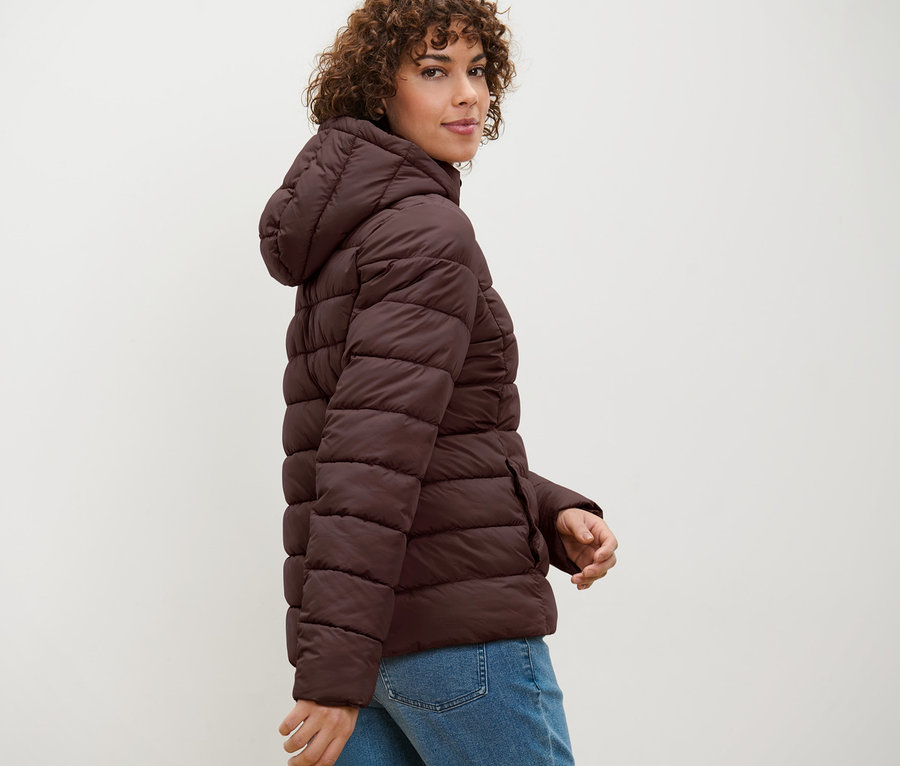 Frau posiert in dunkelbrauner Steppjacke mit Kapuze.