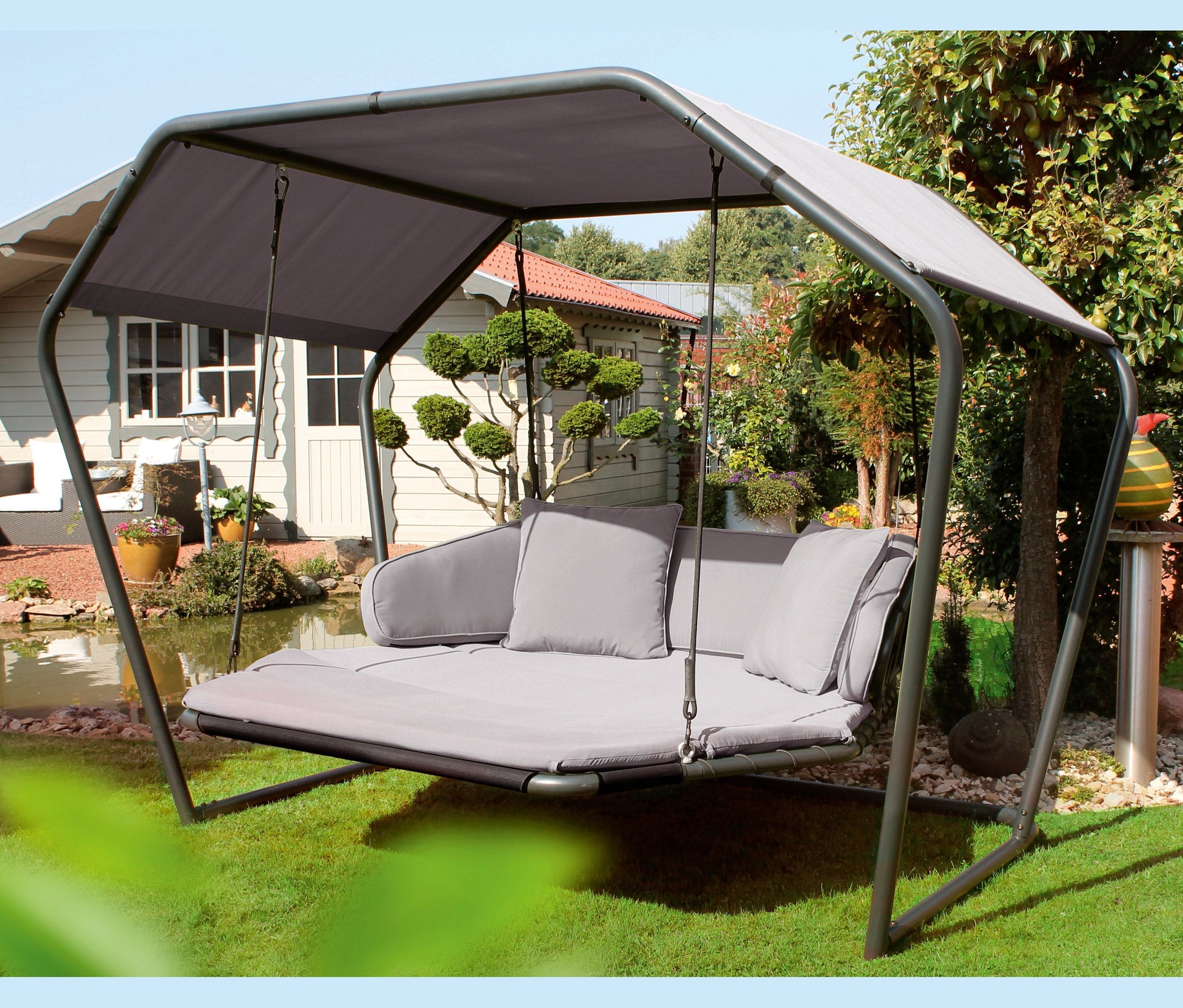Graue Leco Schaukelliege mit Kissen und Überdachung im Garten.