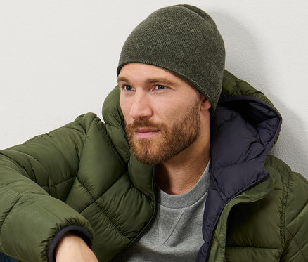 Mann sitzt und trägt eine khaki melierte Strickmütze.