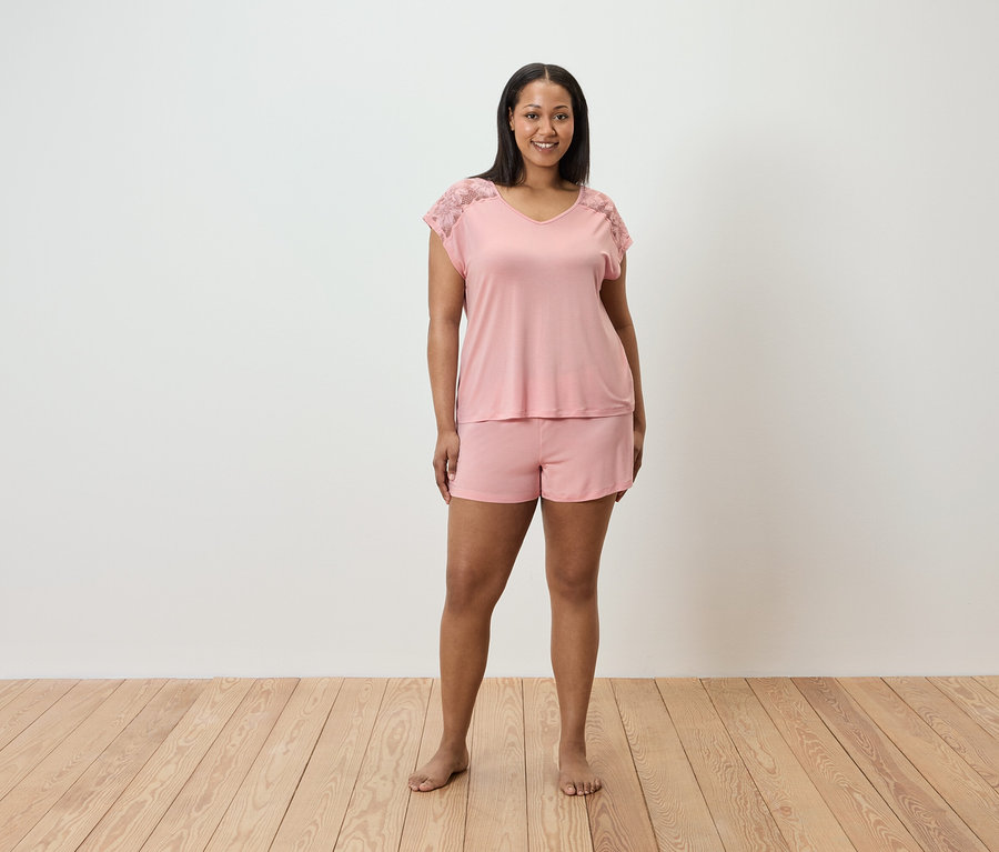 Frau steht und trägt einen rosa Pyjama mit Spitze an den Schultern.