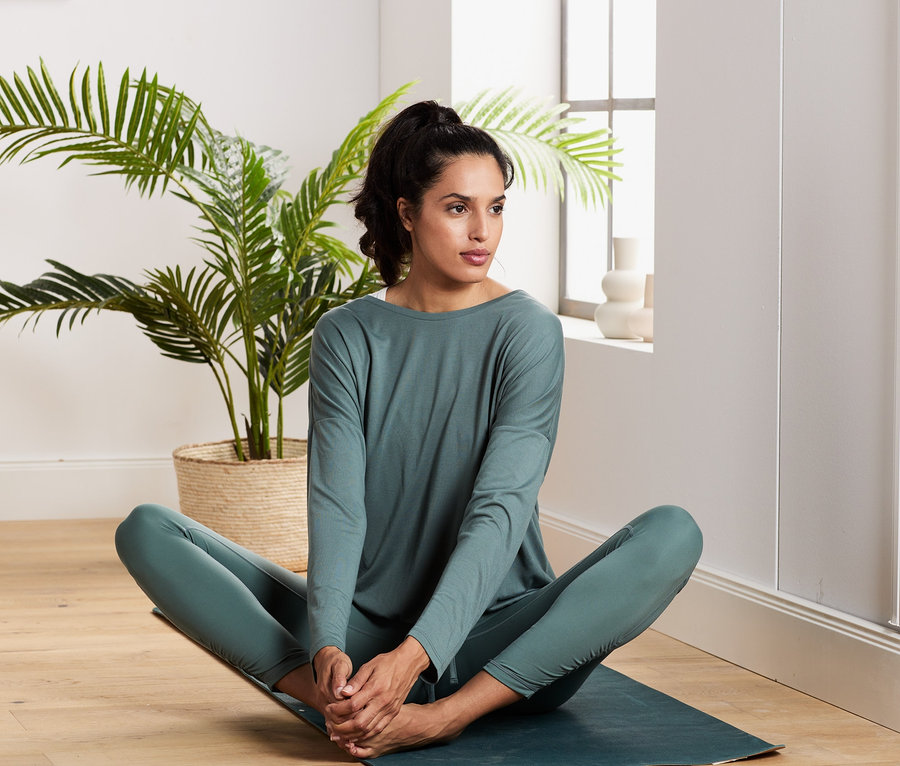 Frau sitzt auf einer Yogamatte und trägt ein grün-weißes 2-in-1-Sportshirt.