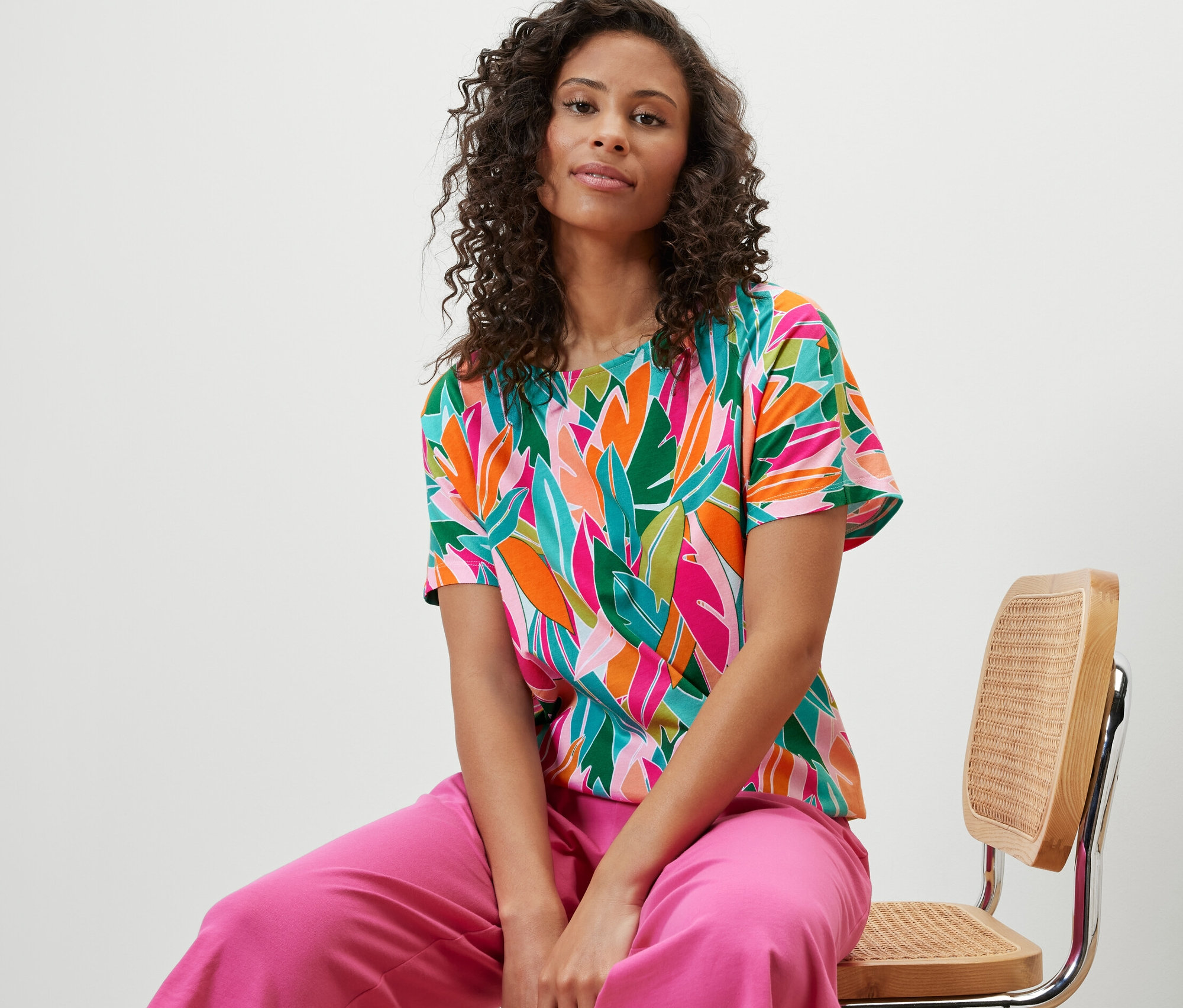 Frau sitzt auf einem Stuhl und trägt ein überschnittenes Blusenshirt mit Alloverprint.