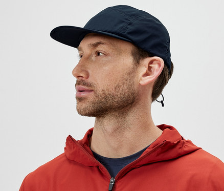Mann in orangefarbener Jacke trägt ein packbares Cap und schaut nach links.