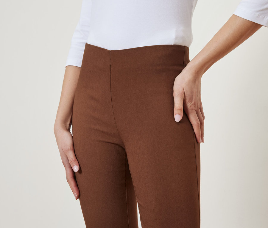 Eine Frau posiert in brauner Hose und weißem Oberteil.